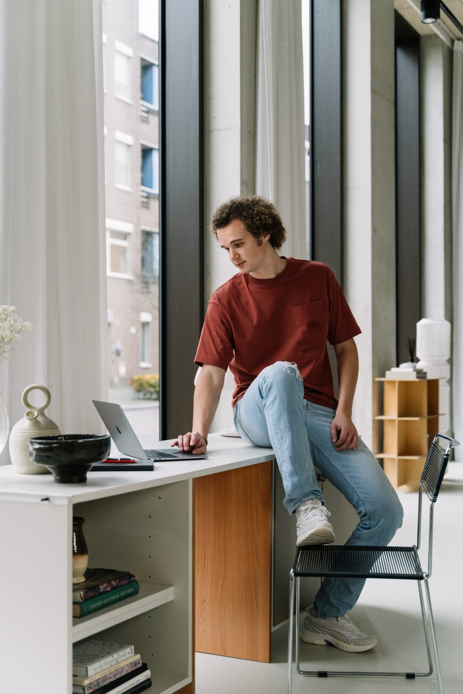 De WBshopmaker zit op een bureau kijkend naar zijn MacBook
