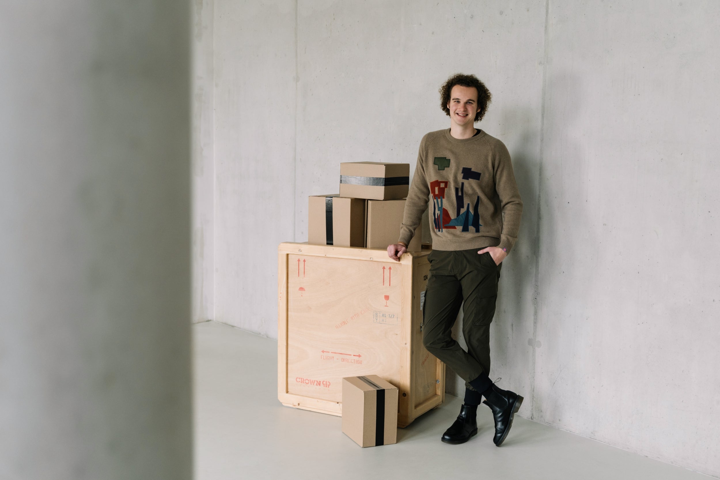 De WBshopmaker naast een houten kist met bestellingen, lachend naar de camera